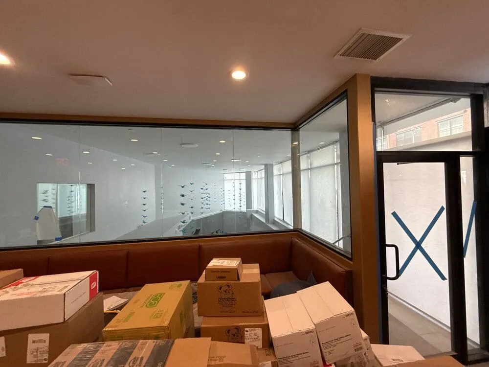 Interior workspace cluttered with boxes and cloudy glass walls, showing how neglected windows can dull even a modern space’s potential.