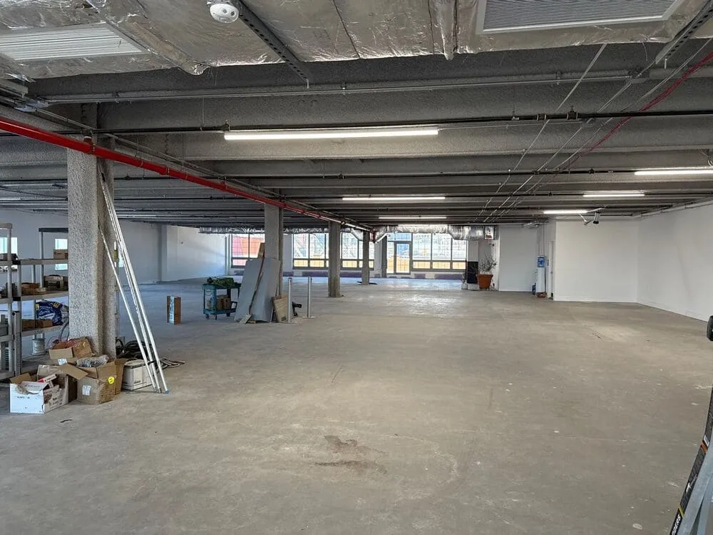 Large open-plan office in renovation, with dusty floors and bare glass, ready to be transformed by professional window cleaning.